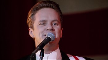 Movie still from “Bob Roberts” (1992), directed by Tim Robbins – A man in a suit is singing into a microphone; Close Up shot, Low angle