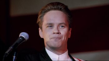 Movie still from “Bob Roberts” (1992), directed by Tim Robbins – A person wearing a suit and tie; Close Up shot, Low angle