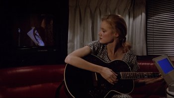 Movie still from “Bob Roberts” (1992), directed by Tim Robbins – A woman sitting on a couch holding a black guitar; Close Up shot, Over the shoulder angle