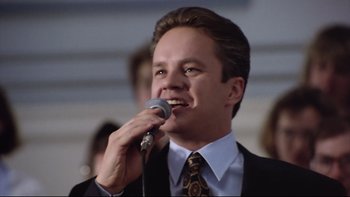 Movie still from “Bob Roberts” (1992), directed by Tim Robbins – A man in a suit and tie holding a microphone up to his mouth; Close Up shot, Low angle