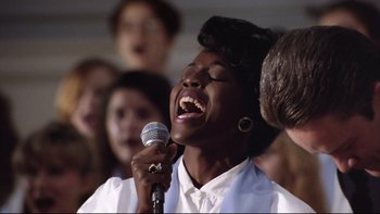 Movie still from “Bob Roberts” (1992), directed by Tim Robbins – A woman singing into a microphone with other people in the background; Close Up shot, Low angle
