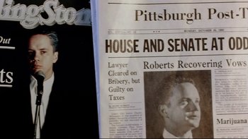 Movie still from “Bob Roberts” (1992), directed by Tim Robbins – A man is smoking a cigarette in front of a newspaper article; Close Up shot, High angle