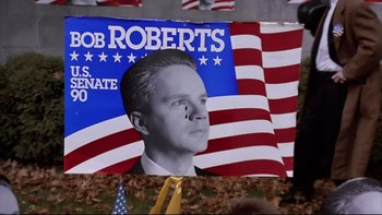Movie still from “Bob Roberts” (1992), directed by Tim Robbins – A political poster of a man with a tie and a flag; Medium shot, Overhead angle