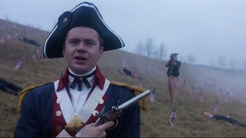 Movie still from “Bob Roberts” (1992), directed by Tim Robbins – A man dressed as an american soldier holding a gun; Medium shot, Low angle