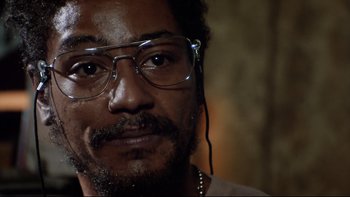 Movie still from “Bob Roberts” (1992), directed by Tim Robbins – A person wearing glasses and a necklace; Close Up shot, Low angle