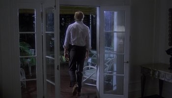 Movie still from “Body Heat” (1981), directed by Lawrence Kasdan – A man in a white dress shirt is walking through a door way; Wide shot, Low angle