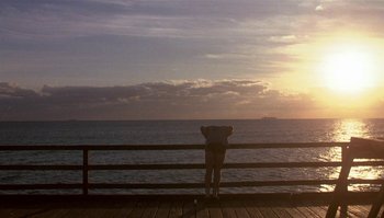 Movie still from “Body Heat” (1981), directed by Lawrence Kasdan – A person standing on a pier looking out at the ocean; Extreme Wide shot, Low angle