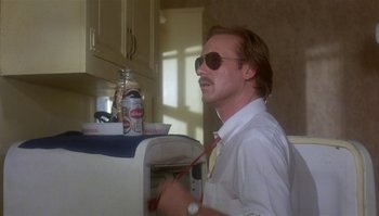 Movie still from “Body Heat” (1981), directed by Lawrence Kasdan – A man in sunglasses and a white shirt is in a kitchen; Medium shot, Low angle