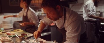 A man in a chef's outfit cutting food in a kitchen