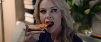 Movie still from “Bombshell” (2019), directed by Jay Roach – A woman eating a piece of pizza while wearing earrings; Close Up shot, Over the shoulder angle
