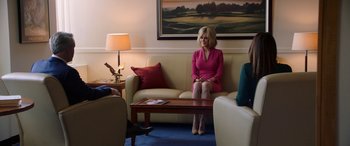 Movie still from “Bombshell” (2019), directed by Jay Roach – A woman sitting on top of a white couch in a living room; Wide shot, Over the shoulder angle