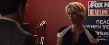 Movie still from “Bombshell” (2019), directed by Jay Roach – A woman in a black and white dress sitting in front of a microphone; Close Up shot, Over the shoulder angle