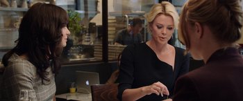Movie still from “Bombshell” (2019), directed by Jay Roach – A woman sitting at a table in front of an open laptop computer; Medium shot, Over the shoulder angle