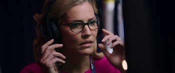 Movie still from “Bombshell” (2019), directed by Jay Roach – A woman wearing glasses and a pink shirt is listening to headphones; Close Up shot, Over the shoulder angle