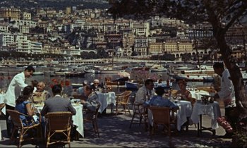 Movie still from “Bon Voyage!” (1962), directed by James Neilson – A group of people sitting at a table with a city in the background; Extreme Wide shot, High angle
