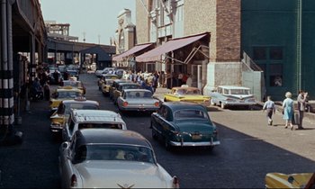 Movie still from “Bon Voyage!” (1962), directed by James Neilson – A street filled with lots of traffic next to tall buildings; Extreme Wide shot, High angle