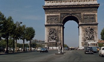 Movie still from “Bon Voyage!” (1962), directed by James Neilson – A couple of people standing in front of an arch on a street; Extreme Wide shot, High angle