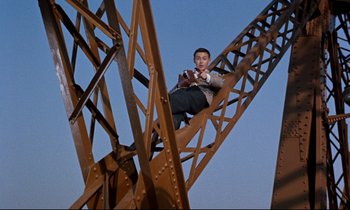 Movie still from “Bon Voyage!” (1962), directed by James Neilson – A man sitting on top of a metal structure; Wide shot, Overhead angle
