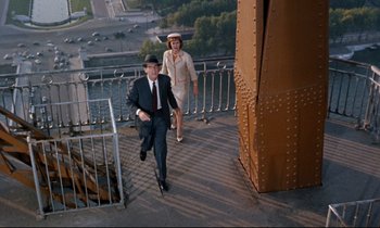 Movie still from “Bon Voyage!” (1962), directed by James Neilson – A man and a woman are walking on a bridge; Wide shot, High angle