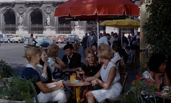 Movie still from “Bon Voyage!” (1962), directed by James Neilson – A group of people sitting at a table in front of an umbrella; Wide shot, High angle