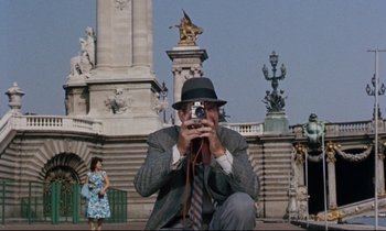 Movie still from “Bon Voyage!” (1962), directed by James Neilson – A man taking a picture with a camera in front of statues; Wide shot, Low angle