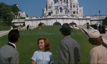 Movie still from “Bon Voyage!” (1962), directed by James Neilson – A man and a woman standing in front of a building; Wide shot, High angle
