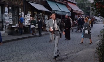 Movie still from “Bon Voyage!” (1962), directed by James Neilson – A man walking down the street holding a camera; Wide shot, High angle