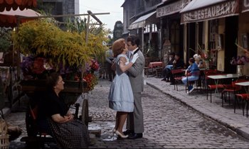 Movie still from “Bon Voyage!” (1962), directed by James Neilson – A man and a woman kissing on the street; Wide shot, Low angle