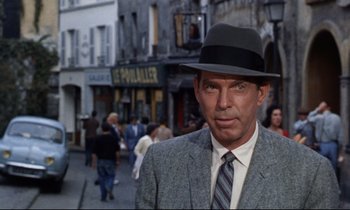 Movie still from “Bon Voyage!” (1962), directed by James Neilson – A person wearing a suit and a hat; Close Up shot, Over the shoulder angle