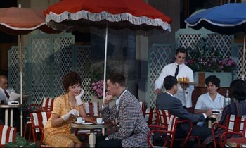 Movie still from “Bon Voyage!” (1962), directed by James Neilson – A man and a woman sitting under an umbrella at an outdoor cafe; Wide shot, High angle