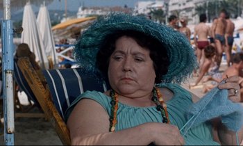 Movie still from “Bon Voyage!” (1962), directed by James Neilson – An older woman sitting on a chair on the beach; Close Up shot, High angle