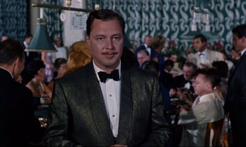 Movie still from “Bon Voyage!” (1962), directed by James Neilson – A man in a suit and bow tie standing in front of a crowd of onlookers; Close Up shot, Low angle
