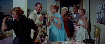 Movie still from “Bonjour Tristesse” (1958), directed by Otto Preminger – A group of people standing around a table with plates of food on top of it; Medium shot, Low angle