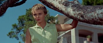 Movie still from “Bonjour Tristesse” (1958), directed by Otto Preminger – A woman in a green and white checkered shirt holding a tree; Medium shot, Low angle
