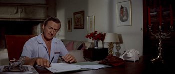 Movie still from “Bonjour Tristesse” (1958), directed by Otto Preminger – A man sitting at a table writing on a piece of paper; Medium shot, High angle