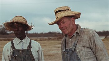 Movie still from “Bonnie and Clyde” (1967), directed by Arthur Penn – Two men in overalls and straw hats standing next to each other in an open field; Medium shot, Low angle