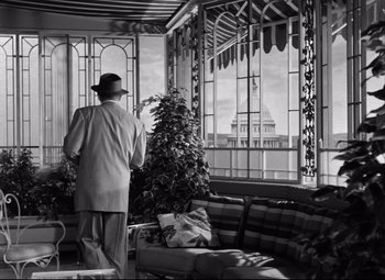 Movie still from “Born Yesterday” (1950), directed by George Cukor – An older man standing in front of a large window; Wide shot, Low angle