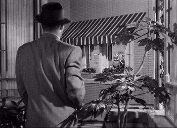Movie still from “Born Yesterday” (1950), directed by George Cukor – A black and white photo of a man looking out of a window; Wide shot, Over the shoulder angle
