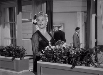 Movie still from “Born Yesterday” (1950), directed by George Cukor – A black and white photo of a woman in a black dress; Medium shot, Over the shoulder angle