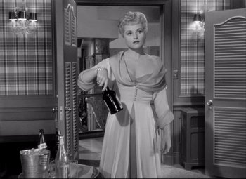 Movie still from “Born Yesterday” (1950), directed by George Cukor – A black and white photo of a woman holding a bottle of wine; Medium shot, Low angle