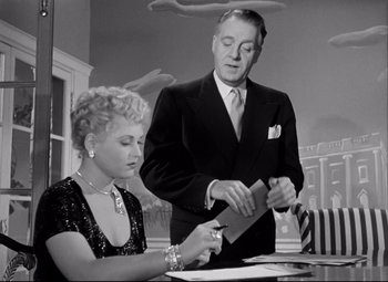 Movie still from “Born Yesterday” (1950), directed by George Cukor – An older man and a young woman look at papers; Medium shot, Low angle