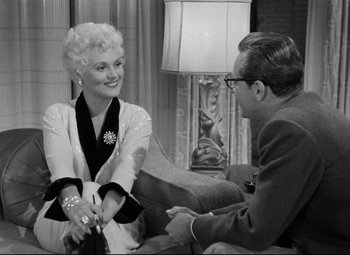Movie still from “Born Yesterday” (1950), directed by George Cukor – An old photo of a man and a woman sitting on a couch; Medium shot, Over the shoulder angle