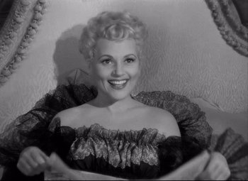 Movie still from “Born Yesterday” (1950), directed by George Cukor – A black and white photo of a woman smiling; Medium shot, High angle