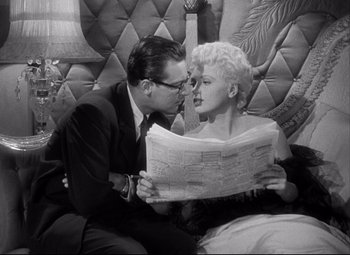 Movie still from “Born Yesterday” (1950), directed by George Cukor – A man and a woman sitting on a couch looking at a newspaper; Medium shot, High angle
