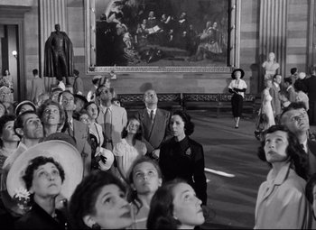 Movie still from “Born Yesterday” (1950), directed by George Cukor – A group of people standing in front of a large painting; Wide shot, Low angle