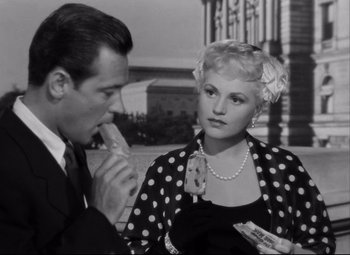 Movie still from “Born Yesterday” (1950), directed by George Cukor – A man and a woman sitting next to each other in front of a building; Medium shot, High angle