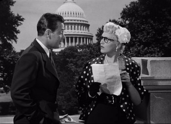 Movie still from “Born Yesterday” (1950), directed by George Cukor – A man and a woman standing next to each other holding papers; Medium shot, Over the shoulder angle