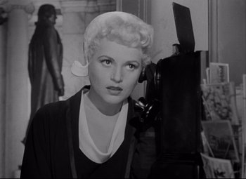 Movie still from “Born Yesterday” (1950), directed by George Cukor – A black - and - white photo of a woman with a camera; Close Up shot, High angle