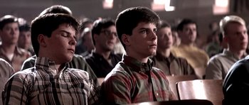Movie still from “Born on the Fourth of July” (1989), directed by Oliver Stone – A group of people sitting in front of a projector screen; Close Up shot, Over the shoulder angle
