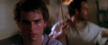 Movie still from “Born on the Fourth of July” (1989), directed by Oliver Stone – A young man is looking into the camera while another man is holding a stick; Close Up shot, Over the shoulder angle